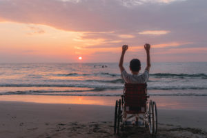 Child with hands up in wheelchair looking at the sunset