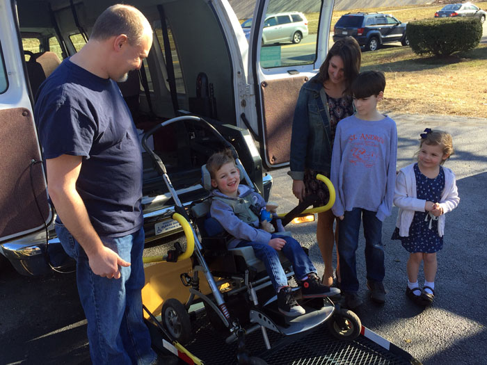 Family with young child in wheelchair next to their donated MagicMobility Van.